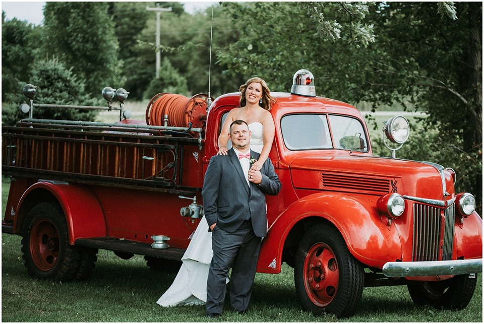 Wedding at The Barn at the Resort at Jellystone Park South Haven with vintage fire truck backdrop Bride and groom posing by a vintage red fire truck at a wedding at The Barn at the Resort at Jellystone Park South Haven