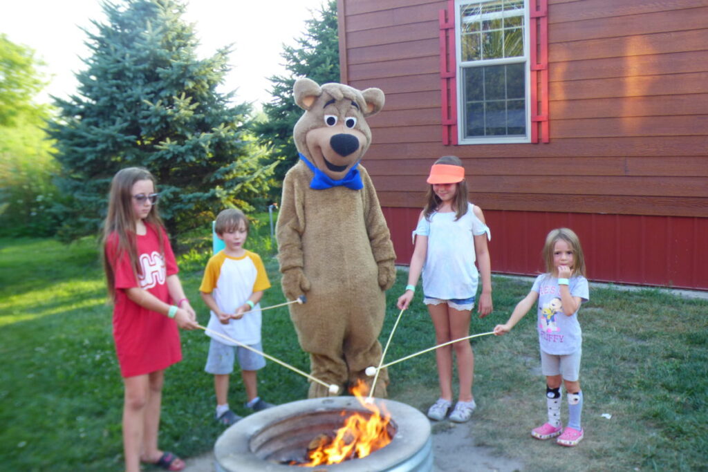 Boo Boo Bear Campfire Fun at Jellystone Park™ South Haven Boo Boo Bear roasting marshmallows with kids around a campfire at Jellystone Park South Haven Michigan